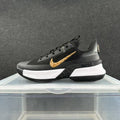 Side view of a black Nike basketball sneaker with a gold-tone Swoosh, white midsole, and black outsole.