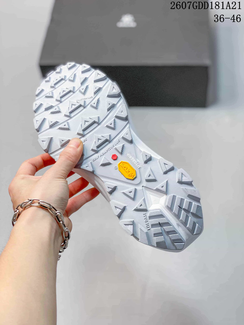 Underside view of the white shoe showing the deep lug pattern, Vibram branding and additional outsole markings.