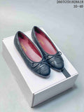 Pair of black quilted Chanel ballet flats with bows displayed on a white shoebox.