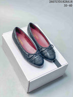 Pair of black quilted Chanel ballet flats with bows displayed on a white shoebox.