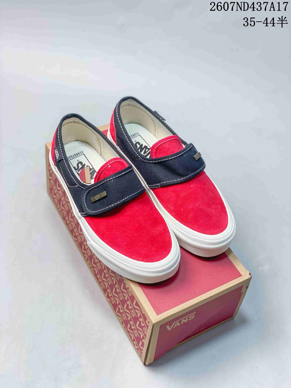 Pair of red and navy Vans slip-on sneakers with wide hook-and-loop straps, shown on a Vans shoebox; size marking 35–44 with half sizes is visible.