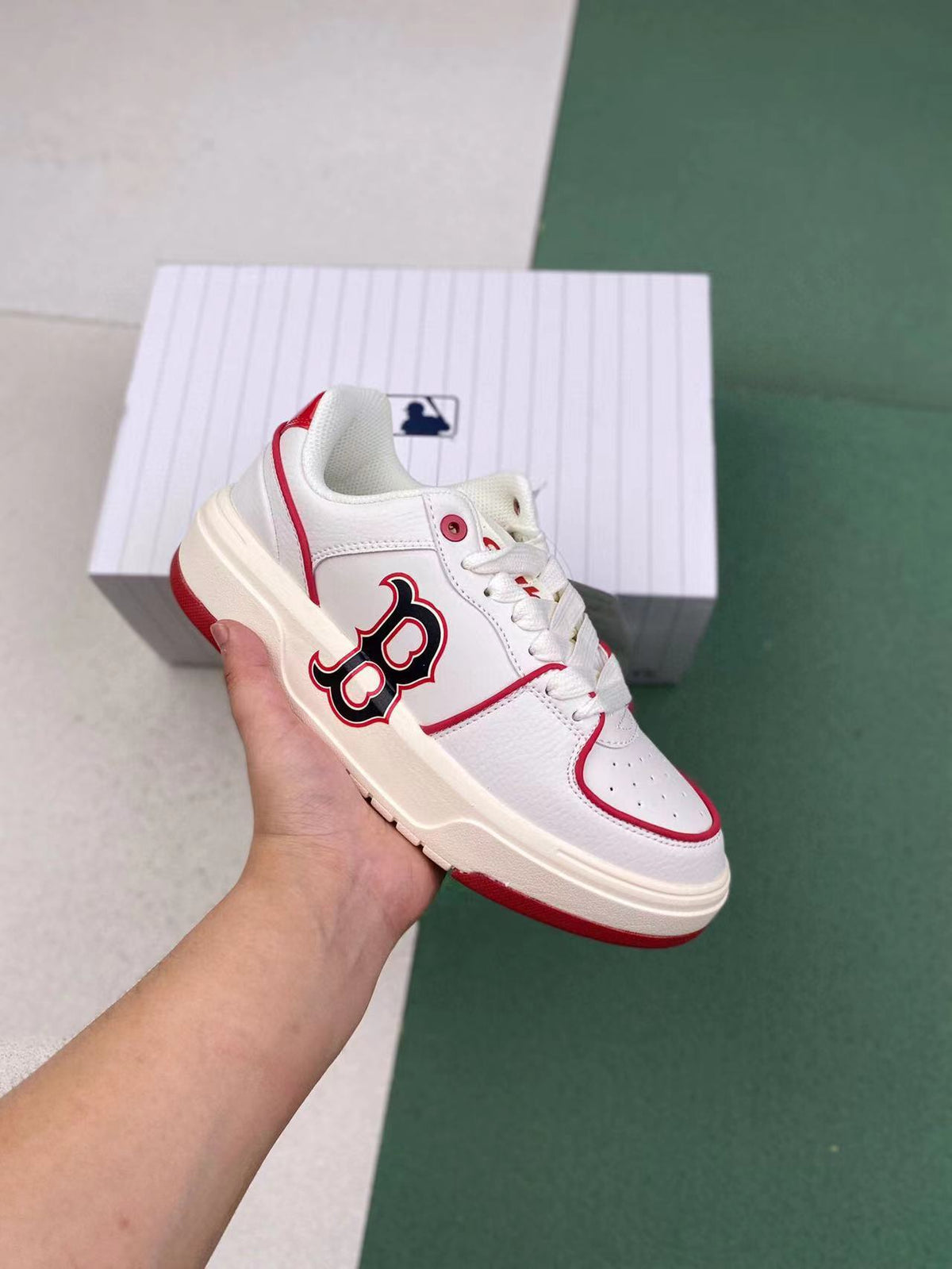 White low-top MLB sneakers with red trim, red outsole accents, and a large side letter emblem, shown with a matching box.