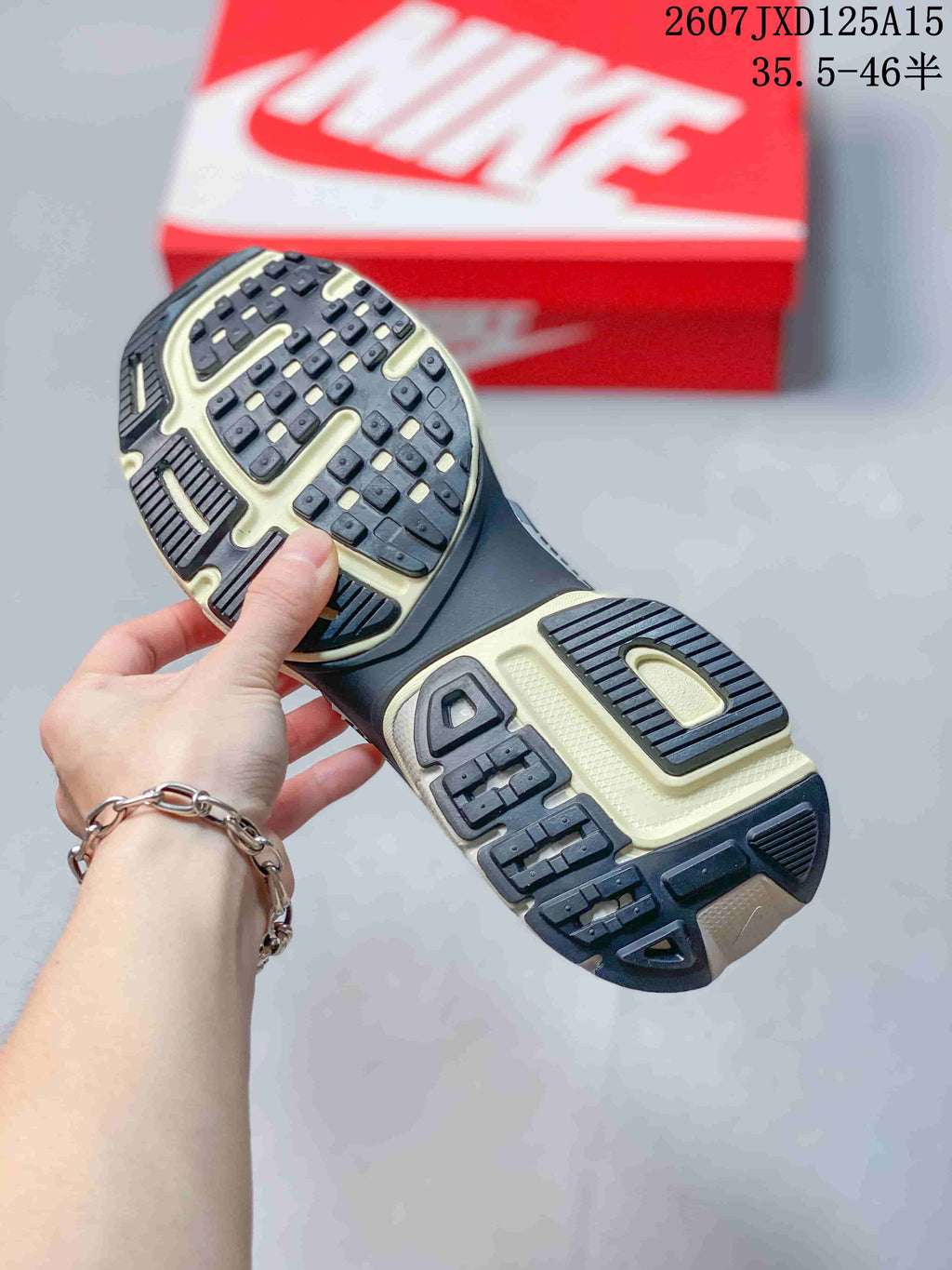 Close view of the sneaker outsole showing black and cream tread sections with raised rubber lugs; a red Nike shoebox is in the background.
