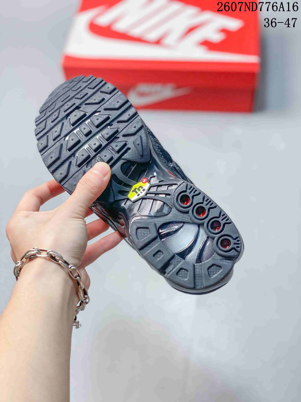 Underside view of a black Nike Air Max Plus sneaker showing the textured rubber outsole and circular midsole cushioning details.