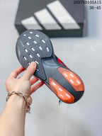 Underside view of the sneaker showing a black outsole with orange rubber sections and elongated traction openings.