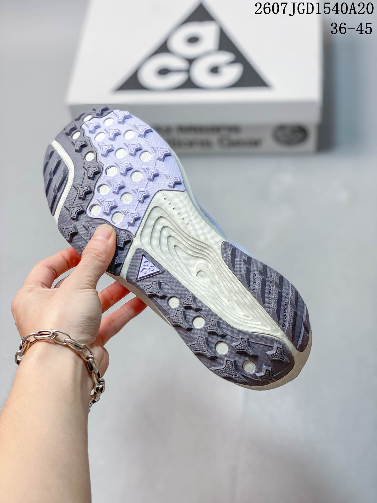 Underside view of a Nike ACG Pegasus Trail sneaker showing the patterned lugged outsole in lavender, gray, and cream tones.