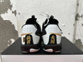 Rear view of white and black Nike basketball shoes with gold heel accents and black, speckled midsoles.