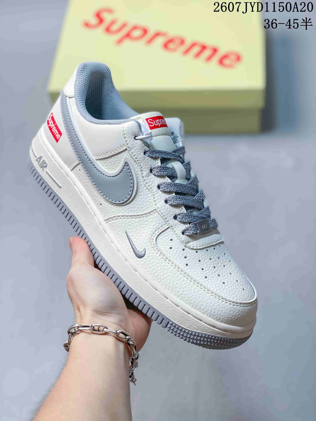 Angled side view of the white and grey sneaker showing the grey Swoosh, Supreme heel accent, Air branding, perforated toe, and grey outsole.