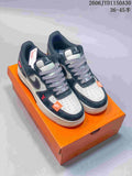 Black and gray low-top sneakers with patterned laces, perforated toe panels, and orange accents on an orange box