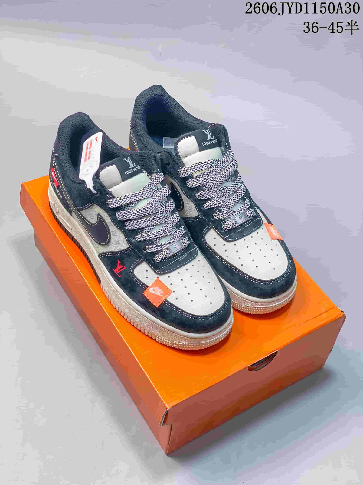 Black and gray low-top sneakers with patterned laces, perforated toe panels, and orange accents on an orange box