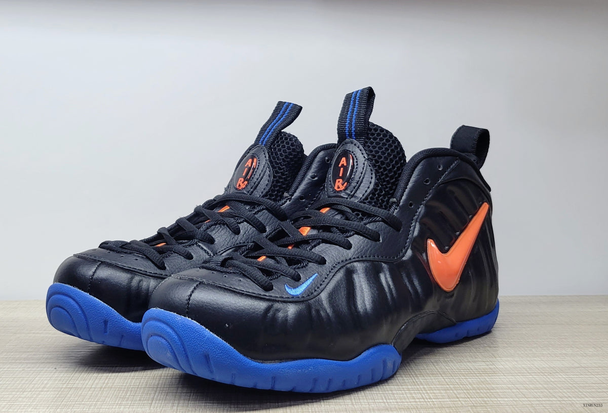 Three-quarter front view of black Nike Air Foamposite Pro high-top sneakers with blue soles and orange accents.