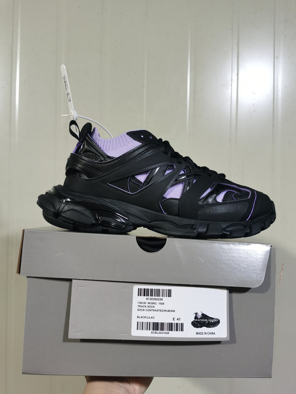 Side profile of the black and lilac sneaker displayed on its box, with the product label visible.