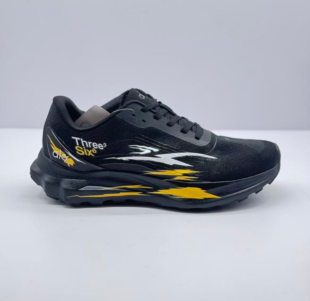 Side view of black Alo Three Six sneaker with white and yellow graffiti-style graphics.