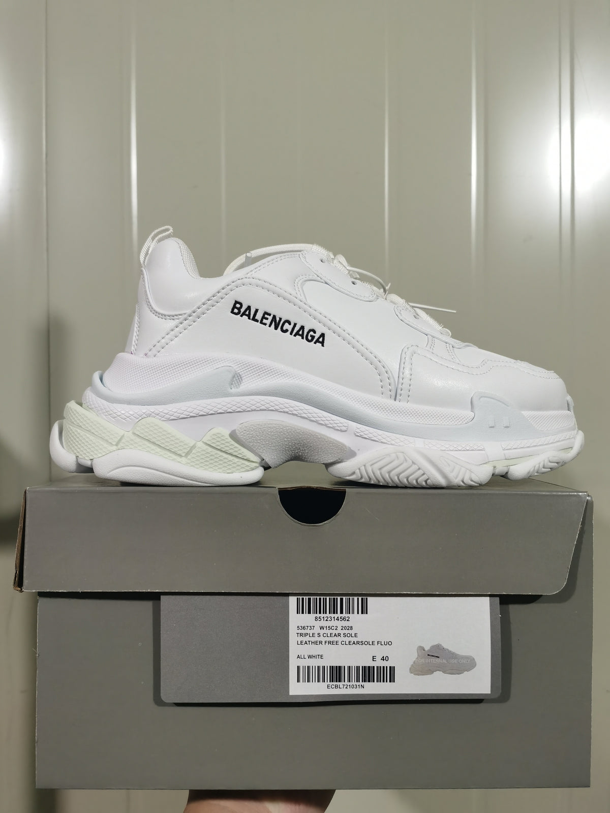 Side view of a white Balenciaga Triple S sneaker resting on its box; the label shows All White, Triple S Clear Sole, and EU 40.