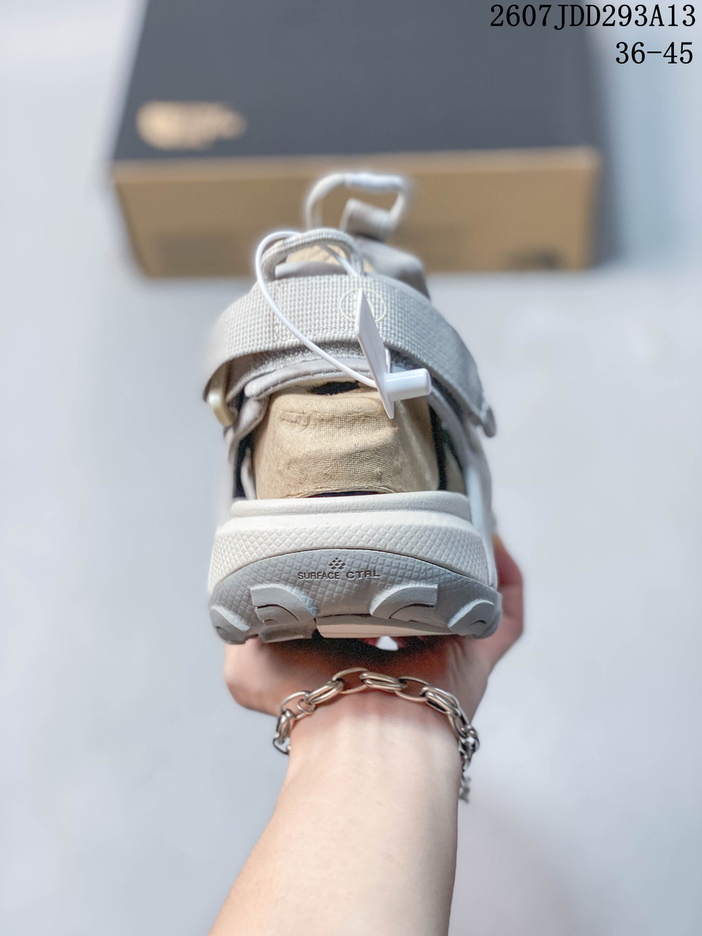 Rear view of a light gray sandal showing the padded heel area, lace toggle, outsole tread, and visible surface-control text.