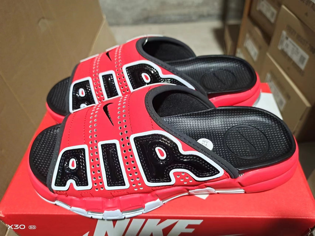 Red and black Nike Air-style slide sandals with contrasting white trim, perforated upper, and segmented outsole.