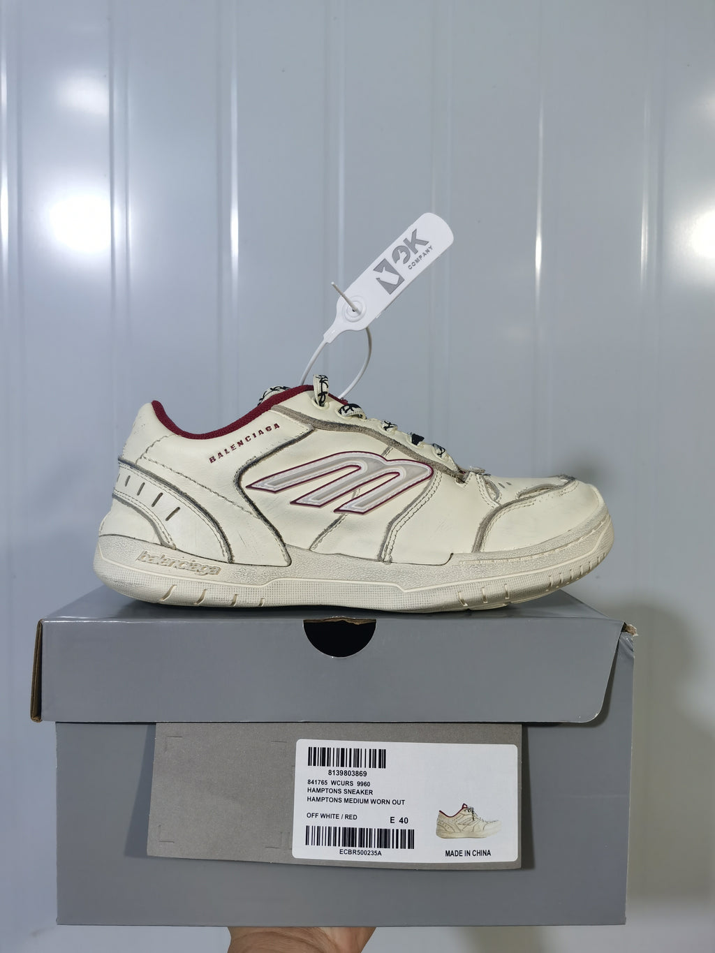 Side view of an off-white Balenciaga Hamptons sneaker with red accents displayed on its box; the box label shows size E 40.
