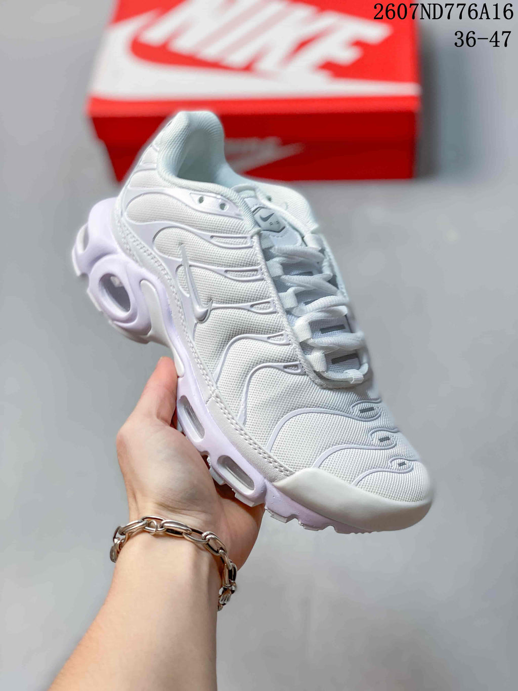 Angled side view of a white Nike Air Max Plus sneaker showing the textured upper, gray Swoosh and segmented sole; style code 2607ND776A16 and size range 36–47 are overlaid.