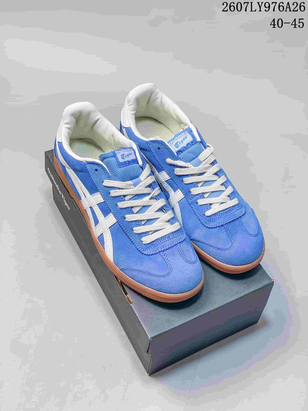 Blue and white Onitsuka Tiger Tokuten sneakers displayed on a black shoe box; image text shows style code 2607LY976A26 and size range 40–45.
