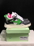 Side view of the sneakers showing the green arrow motif, black and grey layered panels, pink lining and textured off-white outsole.