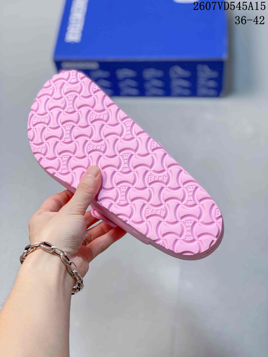 Close view of the pink patterned outsole with repeating embossed motifs; the blue shoe box is visible in the background.