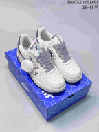 White low-top sneakers with patterned laces, monogram-style side print, and a round lace charm on a blue shoe box.