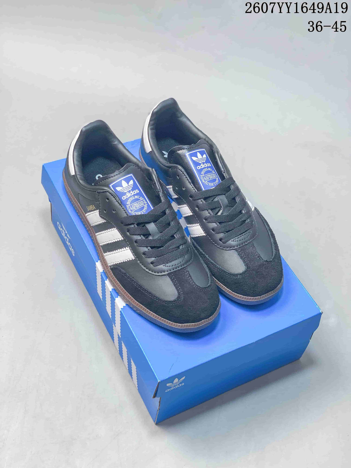 Black Adidas Samba sneakers with white side stripes displayed on a blue shoebox.