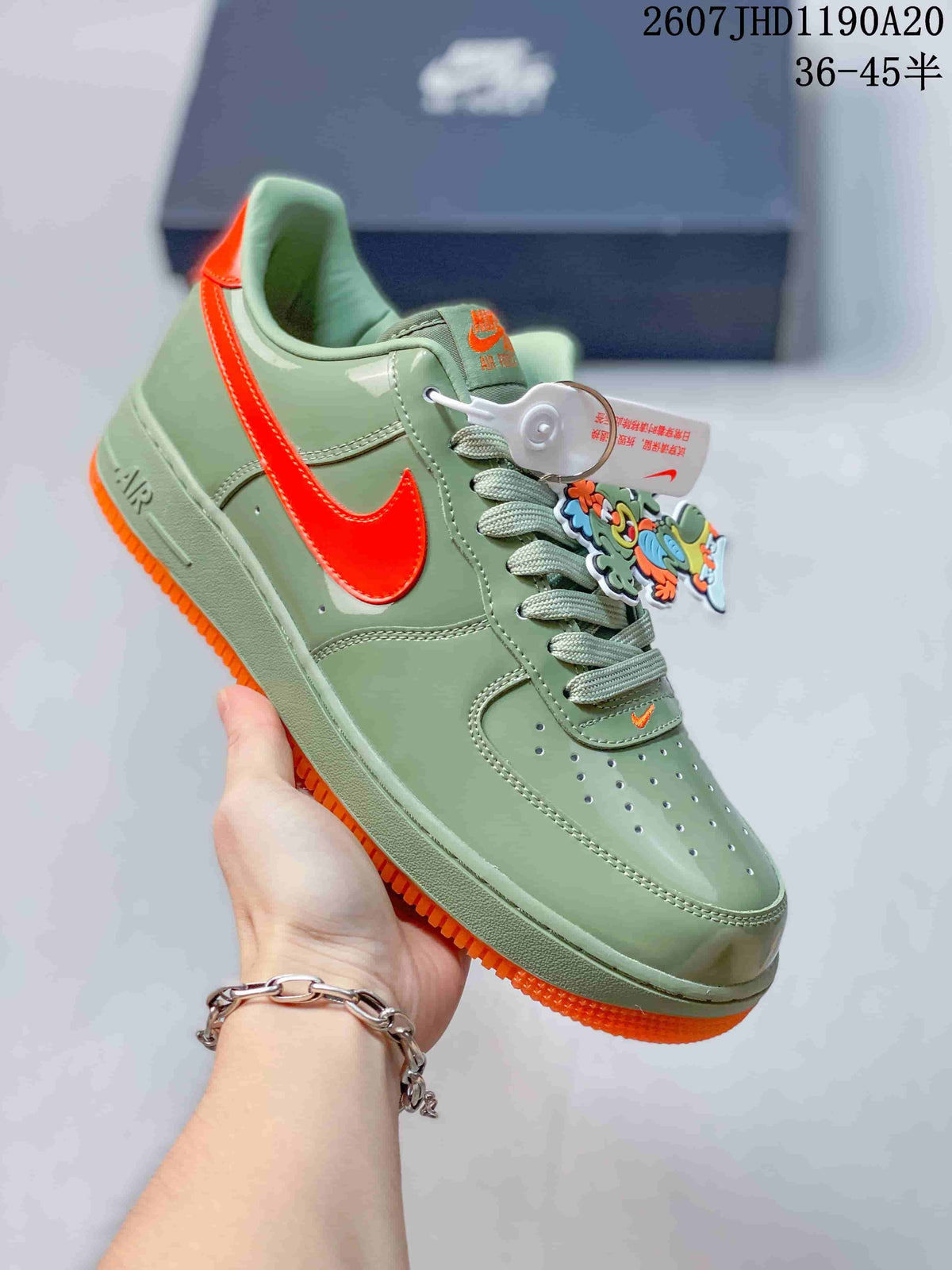 Angled side view showing the green low-top sneaker, bright orange side branding, and orange outsole.