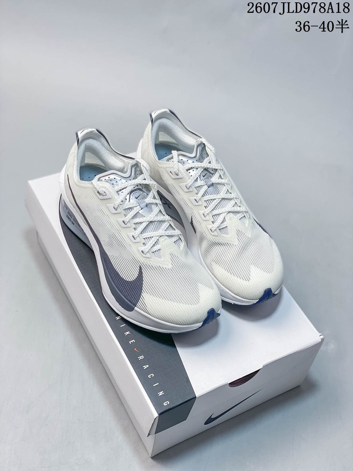 Pair of white and light gray Nike running shoes displayed on a Nike shoe box, with dark navy accents and the code 2607JLD978A18 visible above.