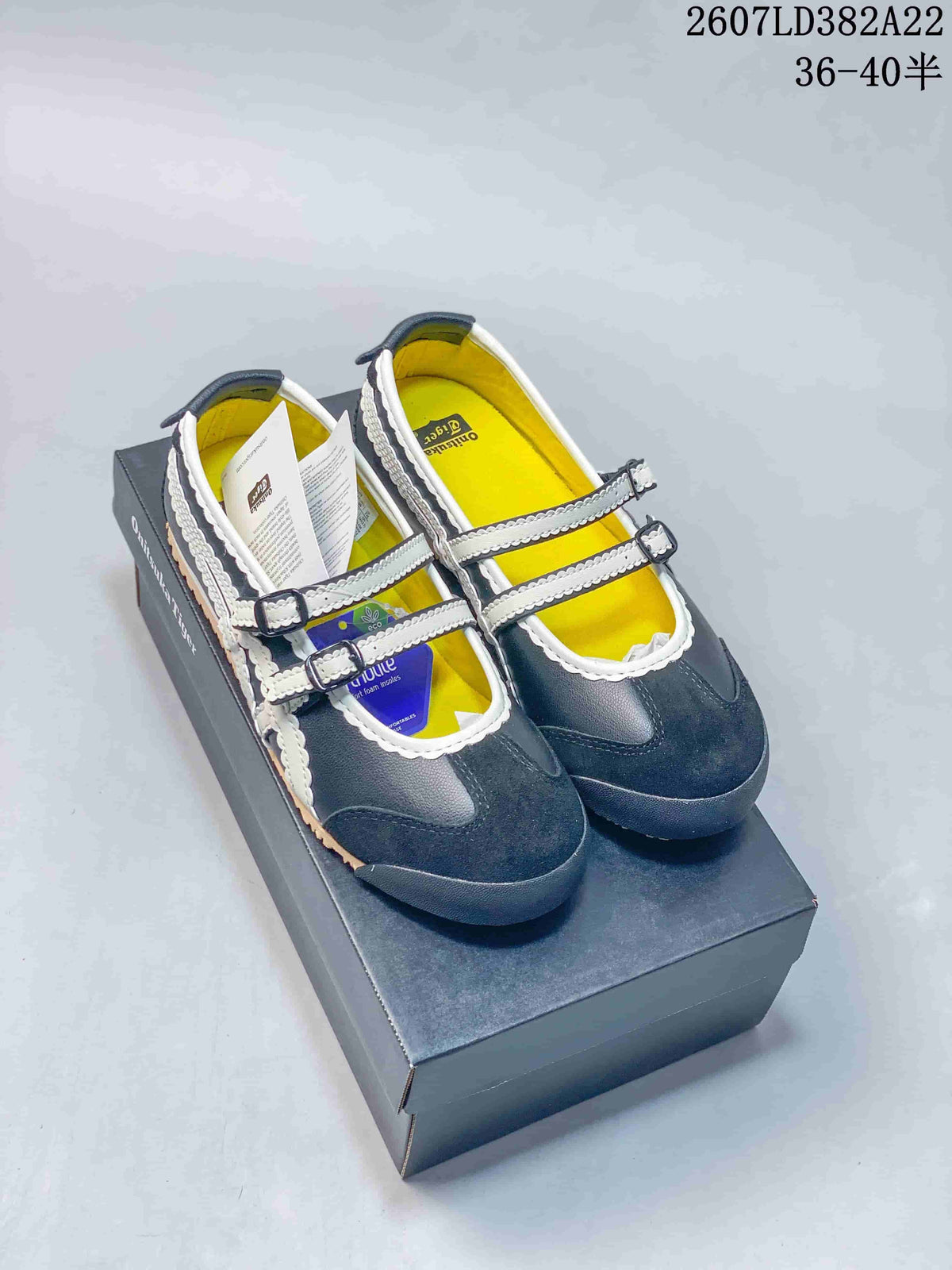 Pair of navy and white Onitsuka Tiger low-top sneakers displayed on a shoebox, with two buckle straps and yellow insoles visible.