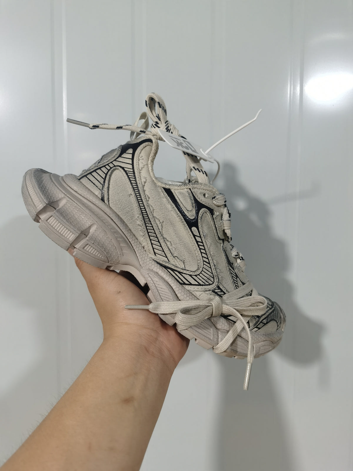 Angled view of the beige and black sneakers highlighting the textured upper, lace arrangement, and chunky outsole.