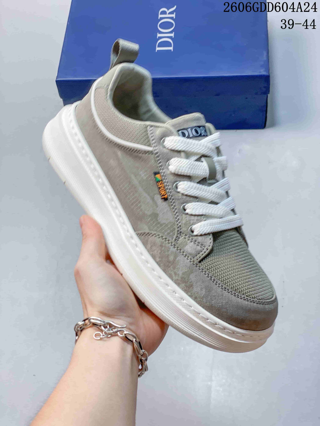 Angled close-up of a gray-green Dior sneaker with visible tongue and side branding