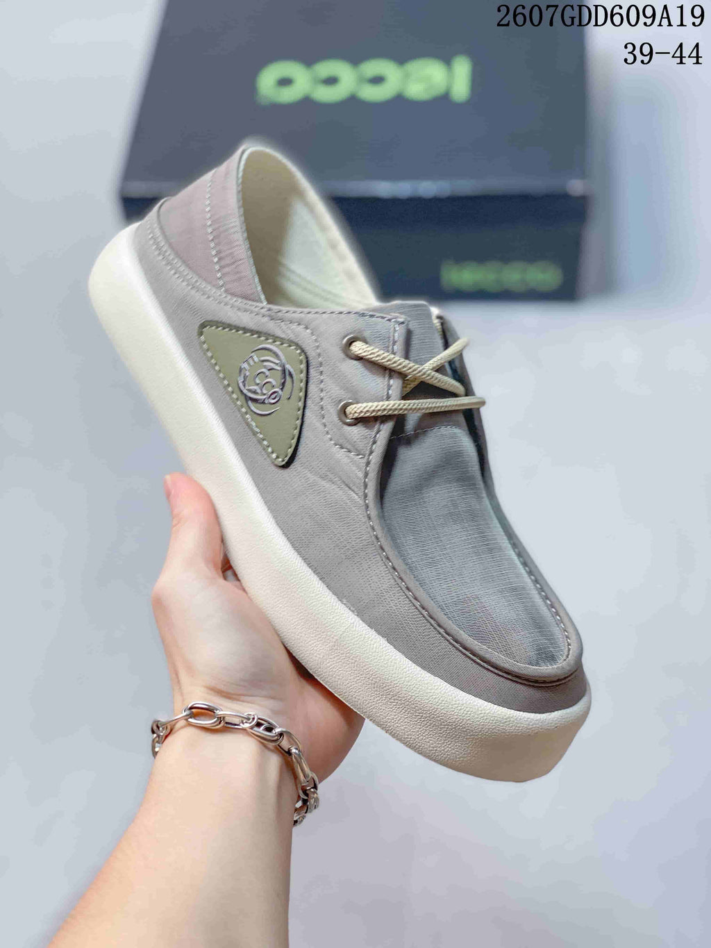 Close-up side view of a gray ECCO lace-up sneaker showing the side emblem, stitched panels and contrasting sole; style code and size range are visible above.