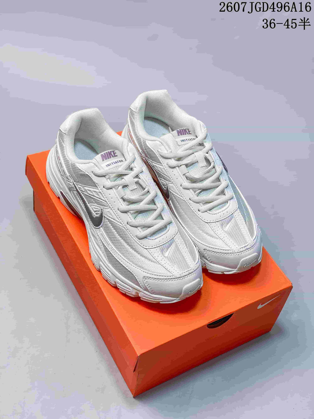 Pair of white and grey Nike Initiator sneakers displayed on an orange shoebox; overlay text shows 36–45 sizing.