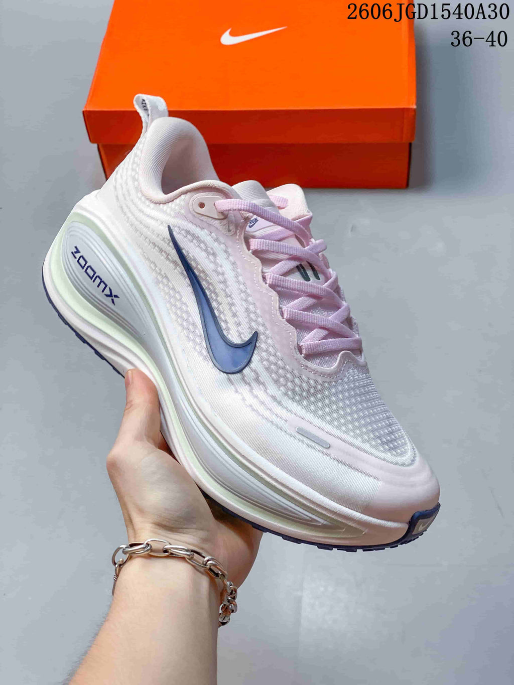 Angled side view of a white and pale pink Nike Vomero Plus running shoe with a blue Swoosh.