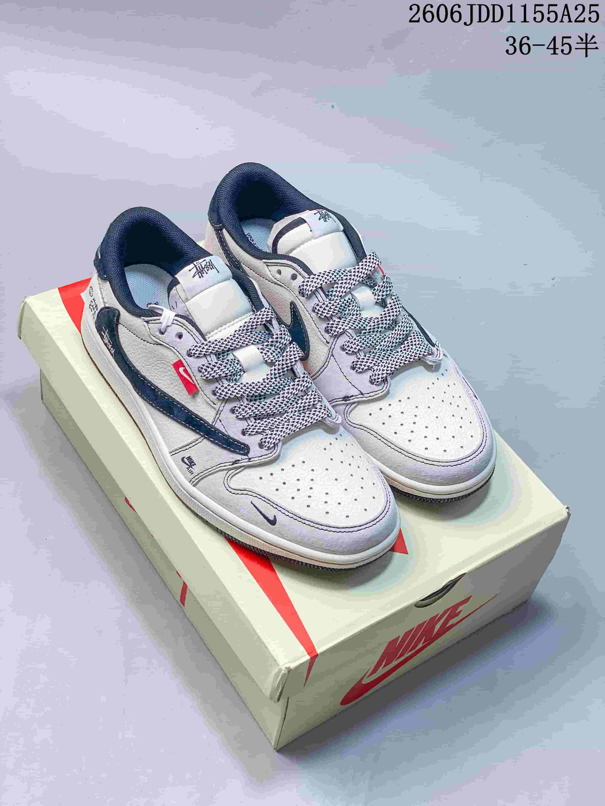 Pair of white and navy low-top sneakers displayed on a branded shoe box, with patterned laces and contrasting Swoosh overlays.