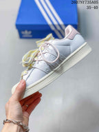 Side view of the white sneaker showing the three-stripe detailing, pink accents, and pastel laces.