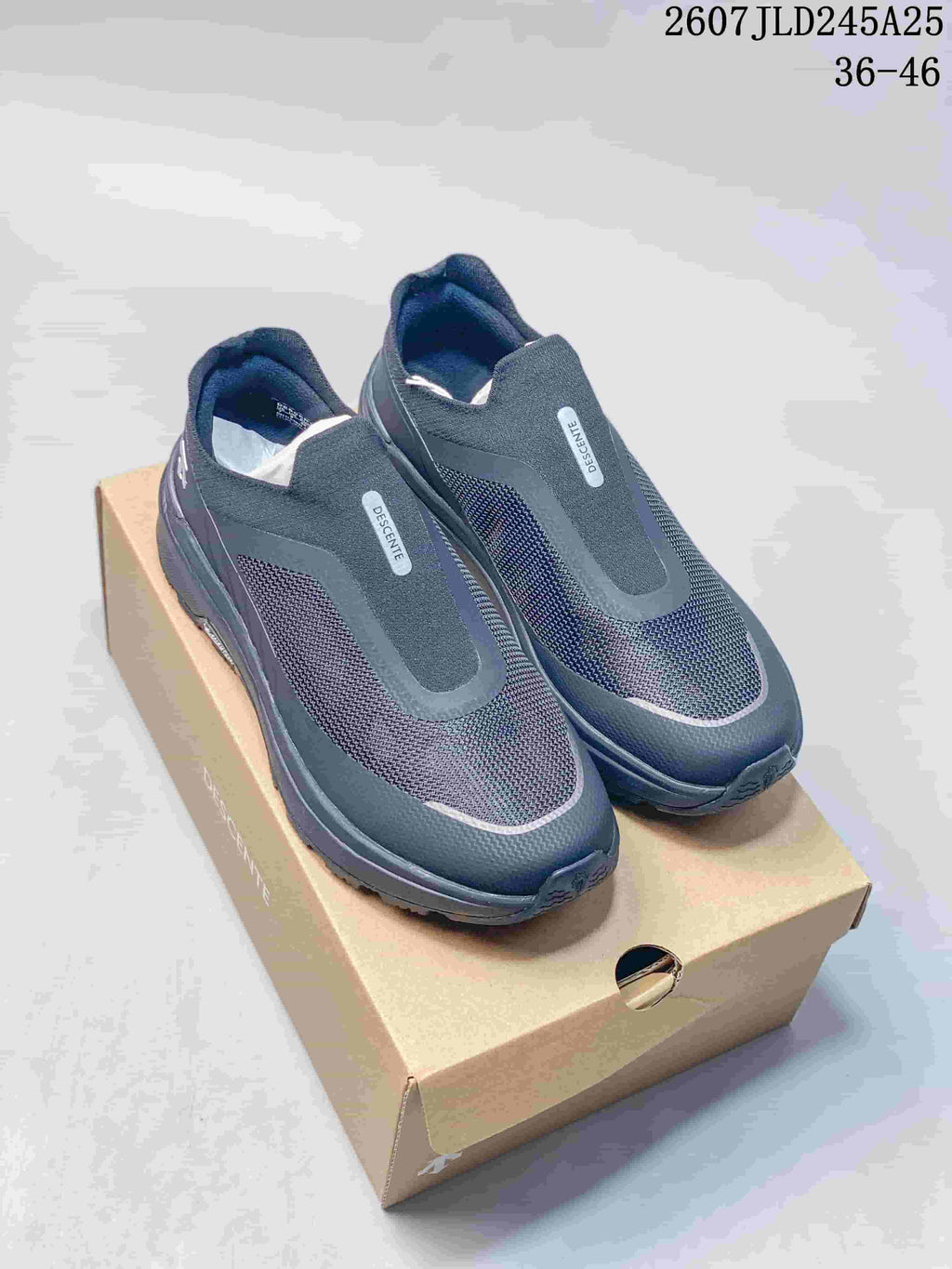 Pair of dark navy and black DESCENTE slip-on sneakers displayed on a shoe box; image text shows style code 2607JLD245A25 and size range 36–46.