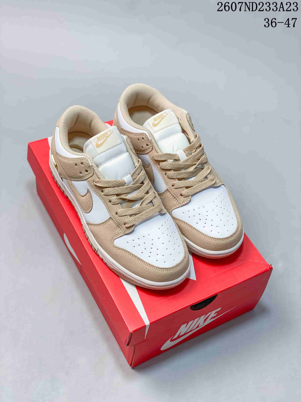 Pair of white and tan Nike low-top sneakers displayed on a red shoebox.