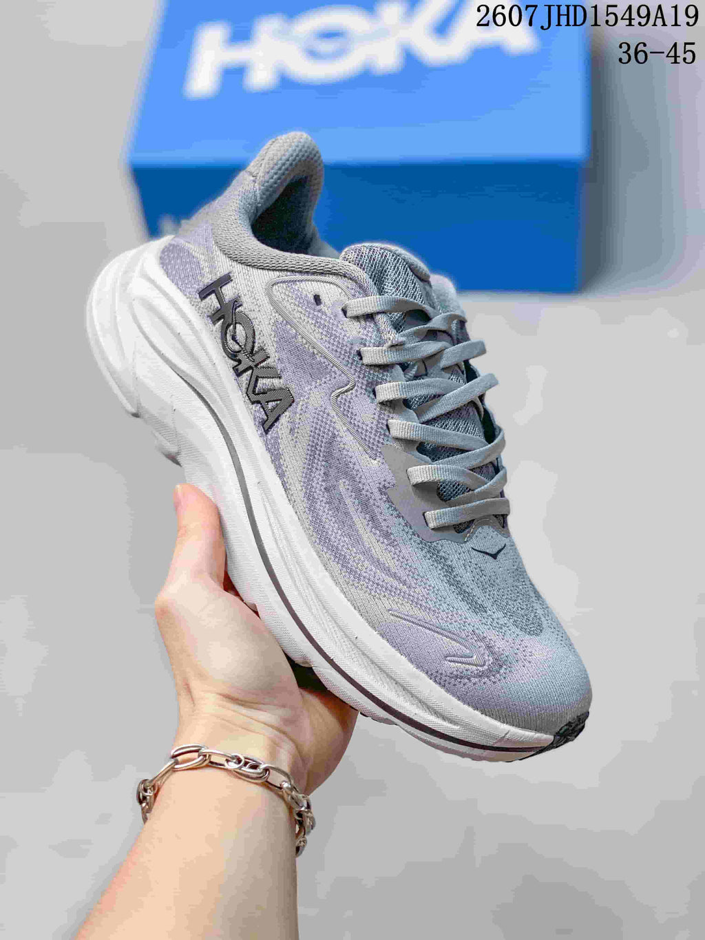 Angled side view of the gray and lavender Hoka sneaker showing the Hoka branding, mesh-style upper, and thick white sole.