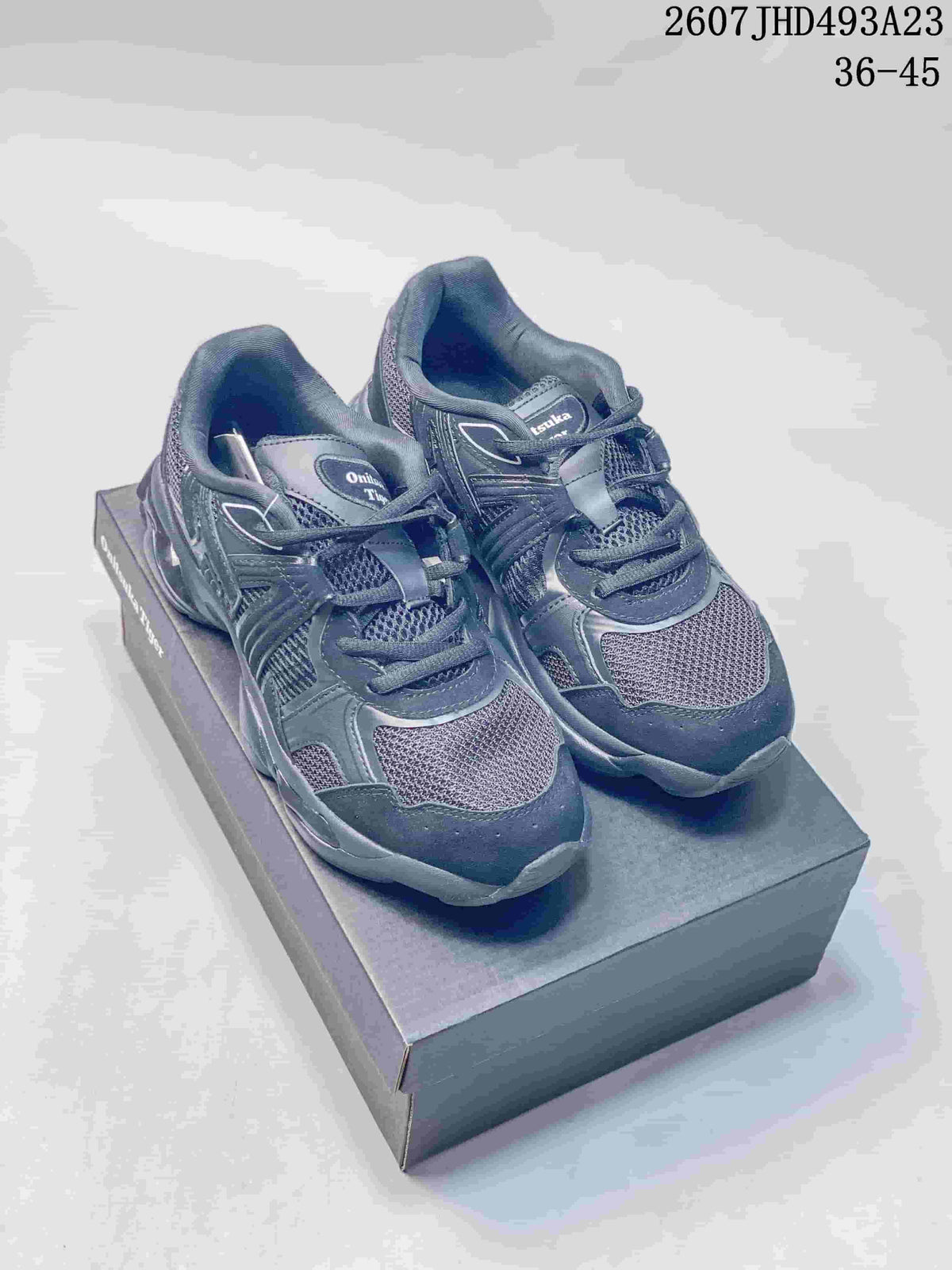 Pair of dark Onitsuka Tiger TIGRUN sneakers displayed on a shoebox, showing the layered upper, mesh panels and chunky sole.