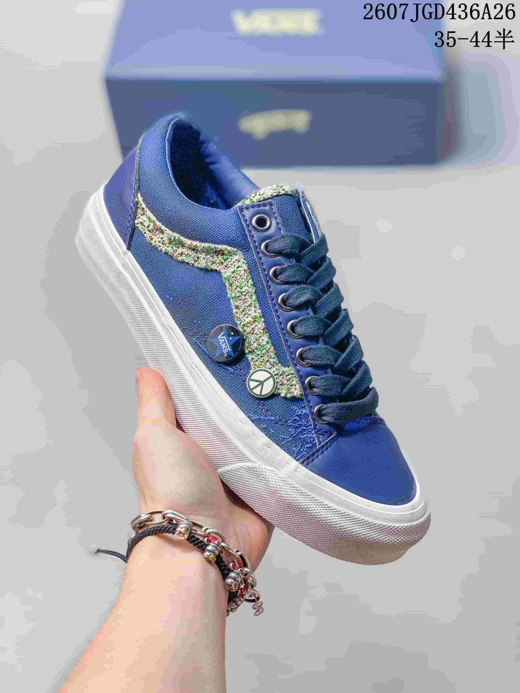 Angled side view of a blue Vans Old Skool sneaker with multicolor stripe, circular side pins, white sole, and blue laces.