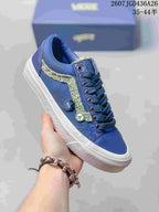 Angled side view of a blue Vans Old Skool sneaker with multicolor stripe, circular side pins, white sole, and blue laces.