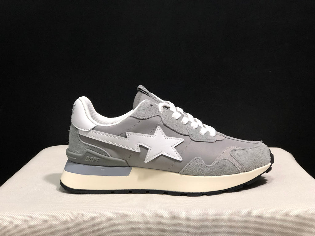 Outer side profile of a grey sneaker showing the white star emblem, BAPE detail near the heel, and black outsole.