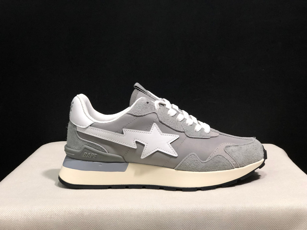 Outer side profile of a grey sneaker showing the white star emblem, BAPE detail near the heel, and black outsole.