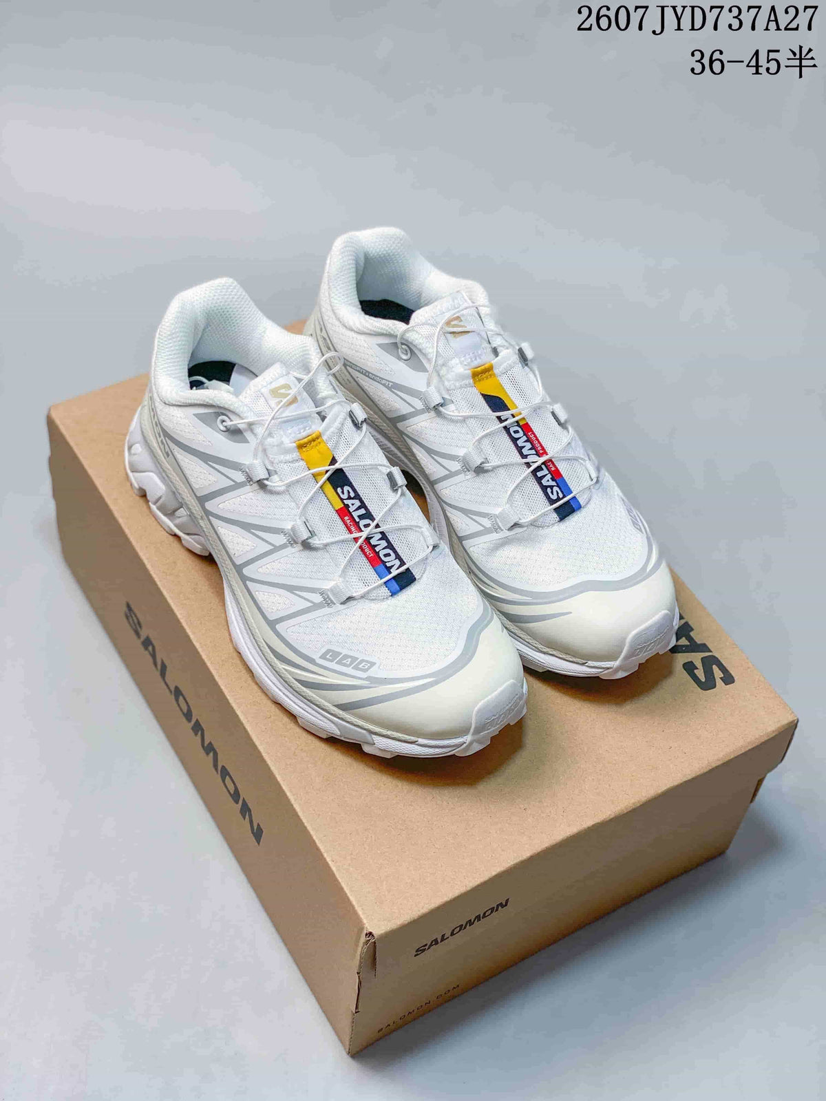 White and gray Salomon XT-6 GTX sneakers displayed on a Salomon shoe box, showing the upper, tongue branding, and cord-style lacing.