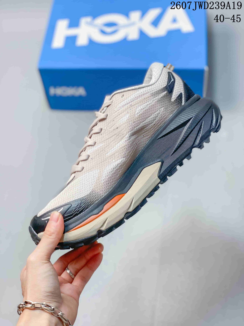 Side view of a low-top HOKA running shoe showing the light upper, dark sculpted midsole, orange accent, and lugged outsole.