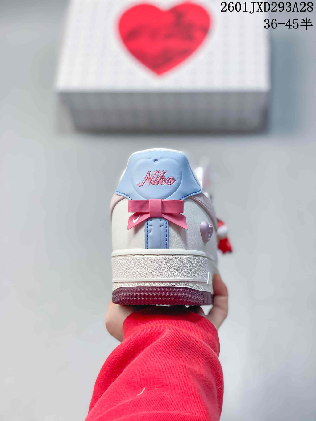 Rear view of a sneaker showing the white heel, pale blue and pink details, bow decoration, and Nike branding.
