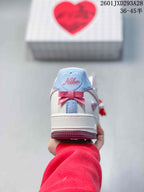 Rear view of a sneaker showing the white heel, pale blue and pink details, bow decoration, and Nike branding.