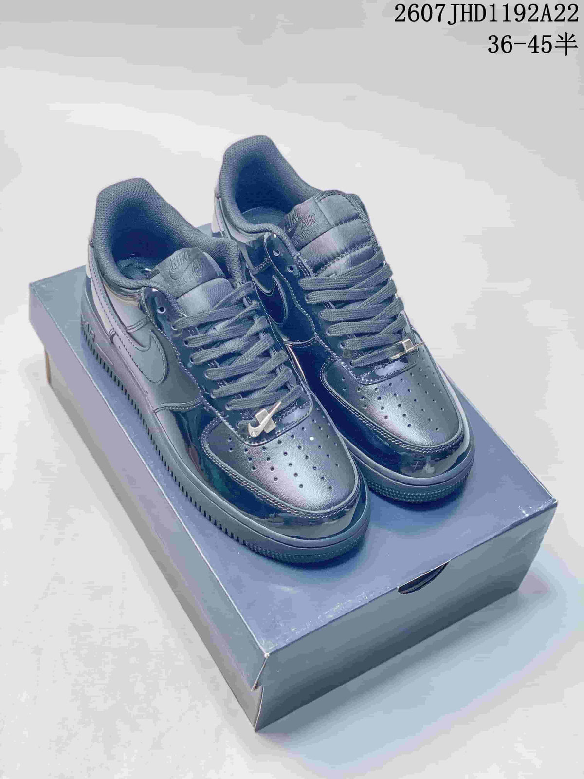 Pair of black Nike low-top sneakers displayed on a shoebox, showing perforated toe boxes, lace-up fronts and swoosh panels.